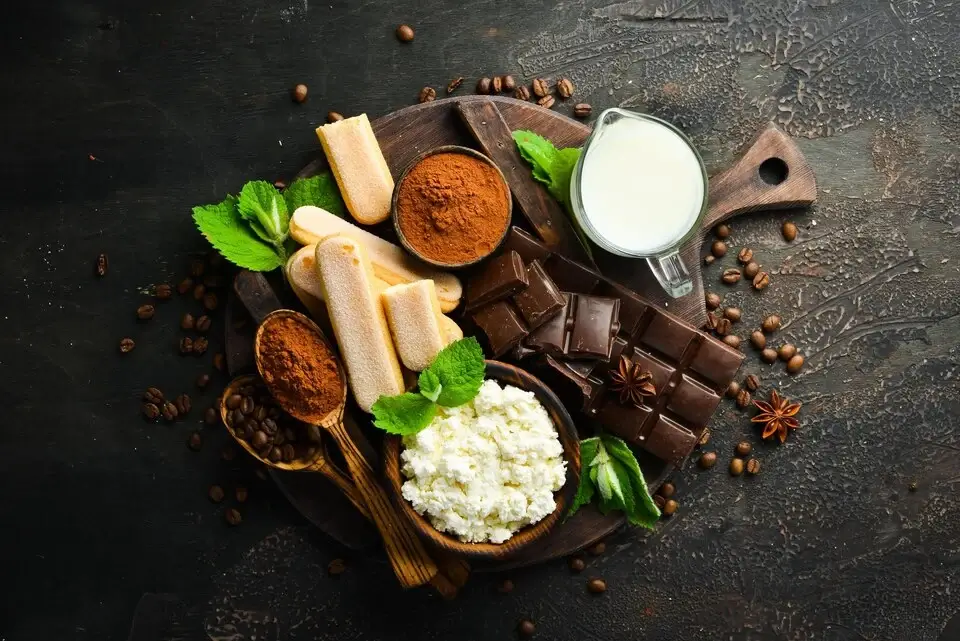 Food items like cheese, milk, chocolate and spices kept in a pan against a dark background